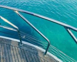 yacht in the open sea. sea with a sandy beach against the backdrop of a mountain. to protect tourists from falling, there is a board made of wood with metal handrails photo