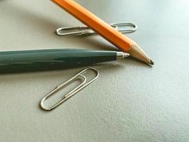 stationery on the table in the office. a blue metal pen for writing, a simple wooden pencil with lead. next to two metal paper clips for documents photo