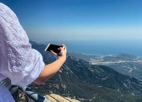 a girl in a white dress with long, dark hair on the observation deck takes a photo of the mountain. observing the texture of rocks. outdoor recreation