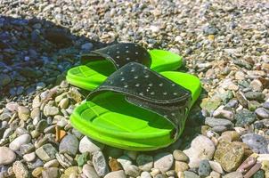 brillantes, verdes, zapatillas de goma están sobre las piedras. vacaciones en el mar, viaje a un país cálido y cálido. los zapatos se paran sobre guijarros mientras su dueño se baña en agua foto