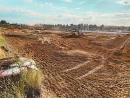 construction field made of sand and mud. a place to build a foundation, a field with traces of a tractor on fresh ground. next to it is a road sign made of metal photo
