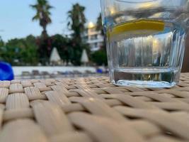 A glass of lemonade with a slice of lemon and mint leaves with ice on a background of palm leaves in a tropical photo