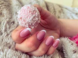 una hermosa mano femenina con uñas rosadas y manicura sostiene un hermoso caramelo rosa delicioso foto