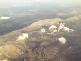 el avión vuela a gran altura con vista a las montañas, piedras, nubes y niebla. vista de la tierra desde arriba. los pasajeros vuelan en un avión con hermosas vistas foto