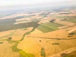 el avión vuela a gran altura sobre un campo vacío, la vegetación y la arena son visibles desde arriba. viajar en avión a otro país extranjero foto