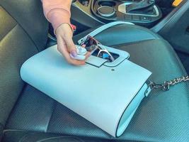 a girl with a pink manicure holds headphones without wires in her hands. flatley. bag and glasses in a car with leather seats. trendy and stylish look. fashion shooting photo