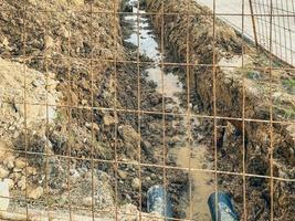 sandy ditch with communications. the moat is protected by a metal mesh in a new microdistrict of the city, pipes are being laid to bring communications to residential buildings photo