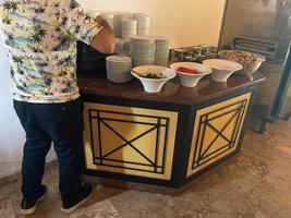 The chef in black apron with a box for a food near the shelf for a buffet with all inclusive it in the hotel in Turkey photo