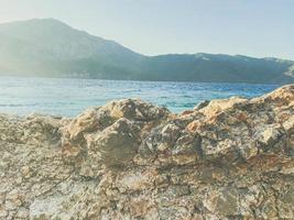 sea coast. mountains and sea in a hot country for recreation. a huge mountain is visible from the beach. stones in the water, rocky shore photo