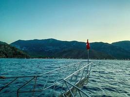 yacht in the open sea. sea with a sandy beach against the backdrop of a mountain, large stones at the bottom. on the yacht a bridge with metal handrails. Turkish flag on the edge photo