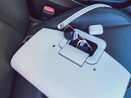 White women's beautiful fashionable leather bag and sunglasses with wireless headphones lie on the leather armchair of a good expensive car photo