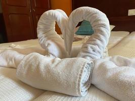 hermoso cisne de toalla de baño blanca decorada en la esquina de la cama y suave luz del sol en el fondo, agradable saludo del hotel foto