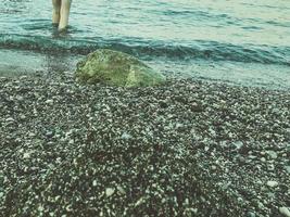 seashore with water and sand. a girl in protective slippers walks along the stones near the shore. tidal bore. wet stones. waves of the sea wash the shore photo