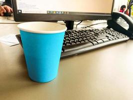 vaso de café turquesa cerca de la computadora. empleado de oficina. teclado y mouse sobre la mesa, teléfono personal con un tubo negro. pausa para el café, almuerzo foto