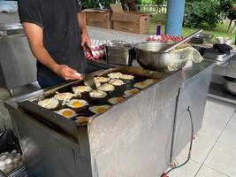 chef, cocinero cocina muchos huevos en la estufa, huevos revueltos en un restaurante en una cocina abierta en un hotel con todo incluido en un complejo turístico de vacaciones en un paraíso tropical cálido foto