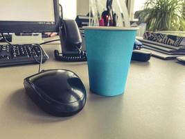 un vaso de café turquesa cerca de una computadora personal. empleado de oficina. teclado y mouse sobre la mesa, teléfono personal con un tubo negro. descanso foto