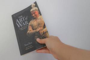 West Java, Indonesia on July 2022. A hand is holding a book called The Art of War by Sun Tzu. photo