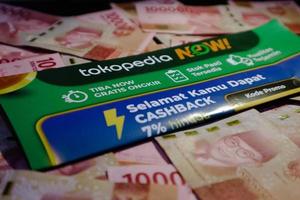 Jakarta, Indonesia in December 2022. A Tokopedia Now flyer above several hundred thousand rupiah notes scattered around. photo