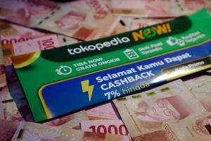 Jakarta, Indonesia in December 2022. A Tokopedia Now flyer above several hundred thousand rupiah notes scattered around. photo