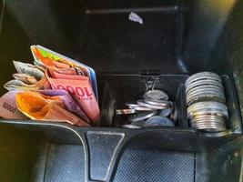 Some rupiah coins and one hundred thousand rupiah notes and some other money in a box provided on the dashboard of the car photo