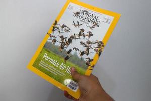 West Java, Indonesia on July 2022. A hand is holding a yellow Indonesian edition of the national geography magazine with the November 2021 photo