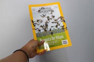 West Java, Indonesia on July 2022. A hand is holding a yellow Indonesian edition of the national geography magazine with the November 2021 photo