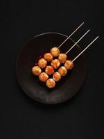 Spicy skewered chicken meatballs on the brown plate in black background photo