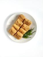 Fried tofu called tahu pong and green chili peppers placed on a ceramic plate isolated on white background. Tahu pong is a type of tofu, popular in Indonesia photo