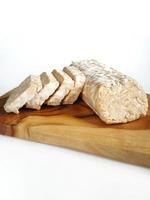 tempe o tempeh en tamaño entero y en cortes más pequeños colocados sobre una tabla de cortar de madera. tomado de la vista frontal. Fondo blanco foto