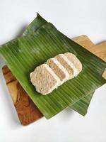 Cut tempeh on banana leaves and wooden cutting board. Tempeh is one of vegetable protein source and having function as prebiotic and probiotic. Isolated on white background. Top view photo