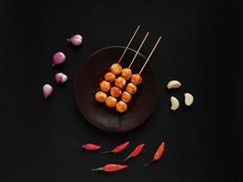 Spicy skewered meatballs garnished with garlics, shallots and red chilies photo