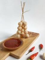 Standing skewered meatballs with spicy sauce on the wooden cutting board garnished with red chilli and garlic photo