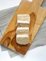 Tempe or tempeh that has been cut into four pieces placed on a wooden cutting board isolated on white background and taken from top view photo