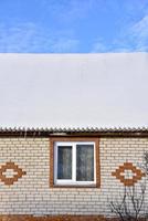 el techo de la casa es de nieve blanca con un cielo azul. el techo de la casa cubierto de nieve en invierno. una casa con ventanas y nieve en el techo. foto