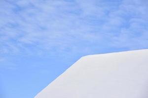 The roof of the house is in white snow with a blue sky. The roof of the house covered with snow in winter. A house with windows and snow on the roof. photo