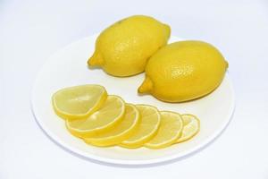 Yellow ripe and juicy fruits of lemons on a white plate. Sliced lemons close-up. Delicious lemons for tea. Lemon slices. photo