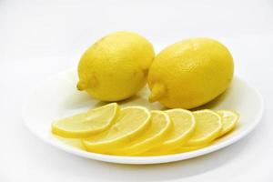 Yellow ripe and juicy fruits of lemons on a white plate. Sliced lemons close-up. Delicious lemons for tea. Lemon slices. photo