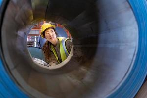 Asian engineer worker is examining the stainless galvanized metal sheet roll inside the warehouse factory for roofing industry concept photo