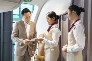 Flight attendant is welcoming and checking passenger boarding pass in business class and show the way to his seat for airplane flight and airline transportation photo