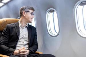 un hombre de negocios caucásico viaja y se sienta cómodamente en el avión mientras mira por la ventana para viajes de negocios en un asiento de clase económica foto