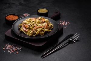 Delicious fresh pasta with pesto sauce and seafood on a black plate photo