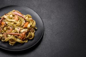 Delicious fresh pasta with pesto sauce and seafood on a black plate photo