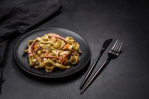 Delicious fresh pasta with pesto sauce and seafood on a black plate photo