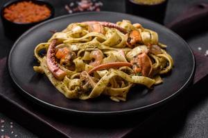 Delicious fresh pasta with pesto sauce and seafood on a black plate photo