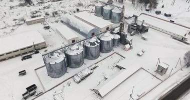 flight over agro silos granary elevator in winter day in snowy field. Silos on agro-processing manufacturing plant for processing drying cleaning and storage of agricultural products video