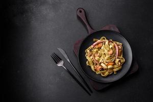 Delicious fresh pasta with pesto sauce and seafood on a black plate photo