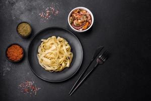 Delicious fresh pasta with pesto sauce and seafood on a black plate photo