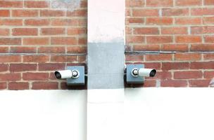 Two surveillance cameras installed on red brick wall. photo