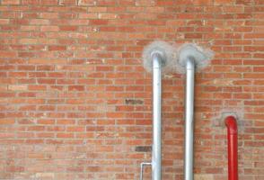 Two silver pipes and red one installed on old red brick wall. photo