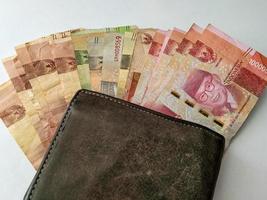 several rupiah bills with a brown wallet and a white background photo